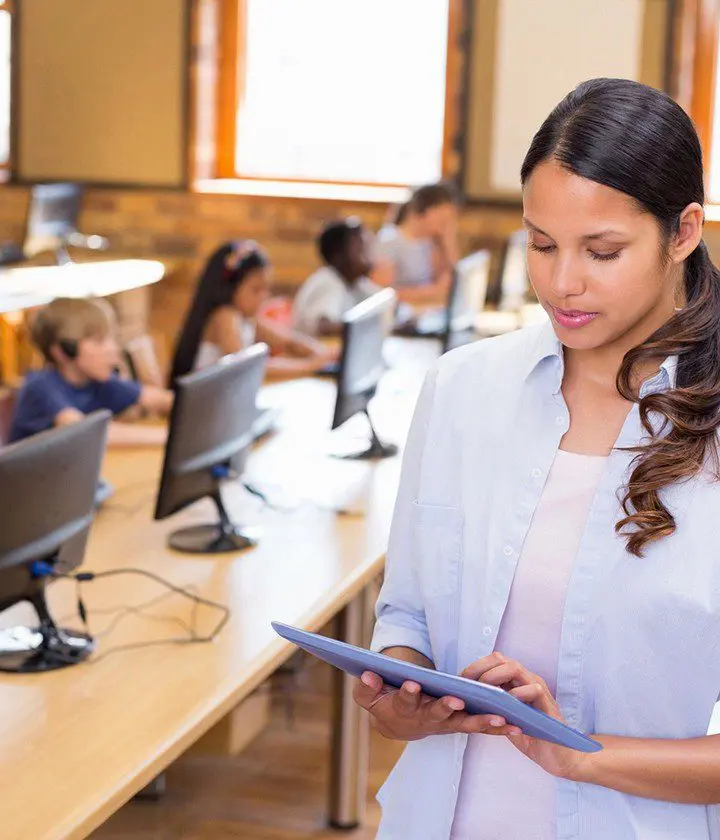 A woman is holding an ipad in front of some computers.