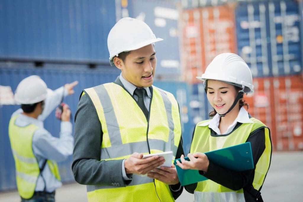 Two people in hard hats and vests looking at a tablet.