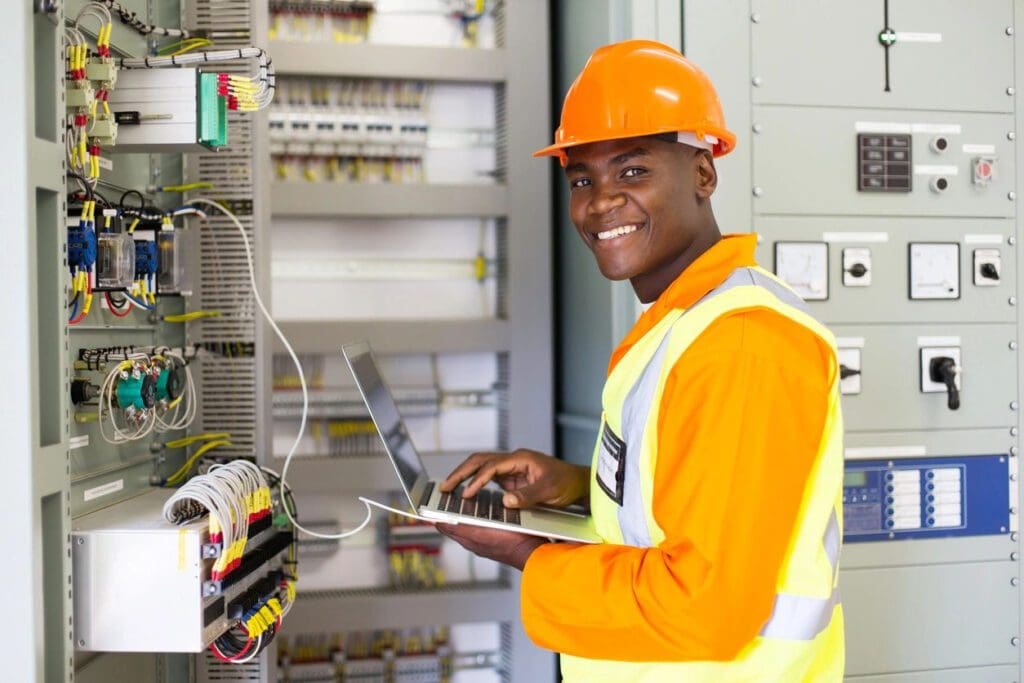 A man in an orange vest and hard hat holding a laptop.