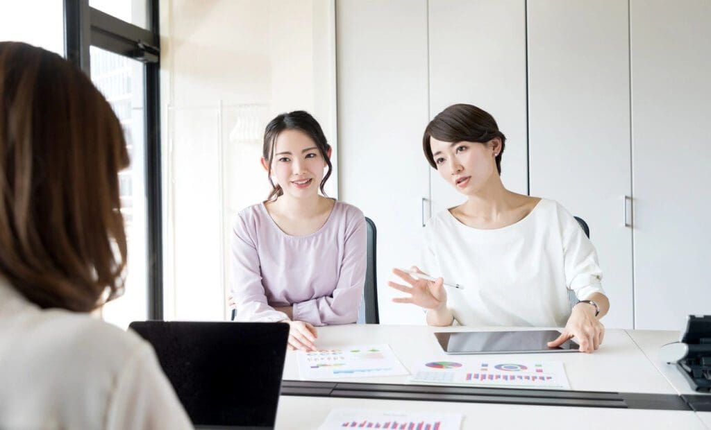 Two women sitting at a table with laptops.