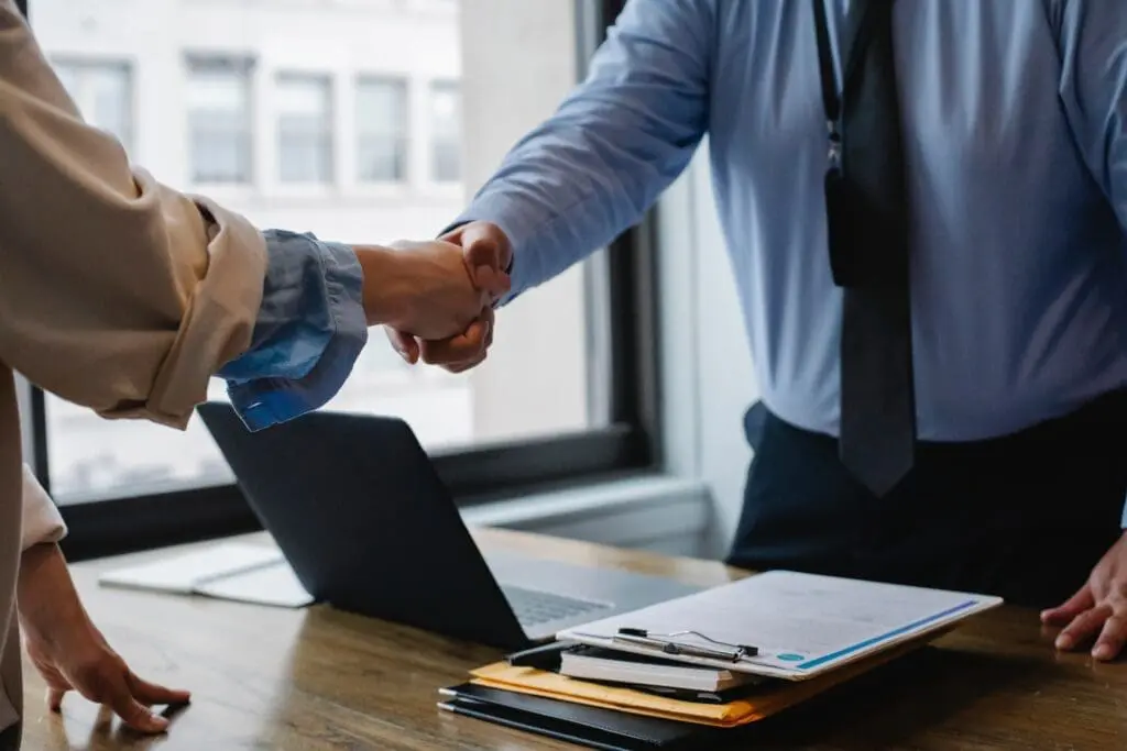 Two people shaking hands over a laptop