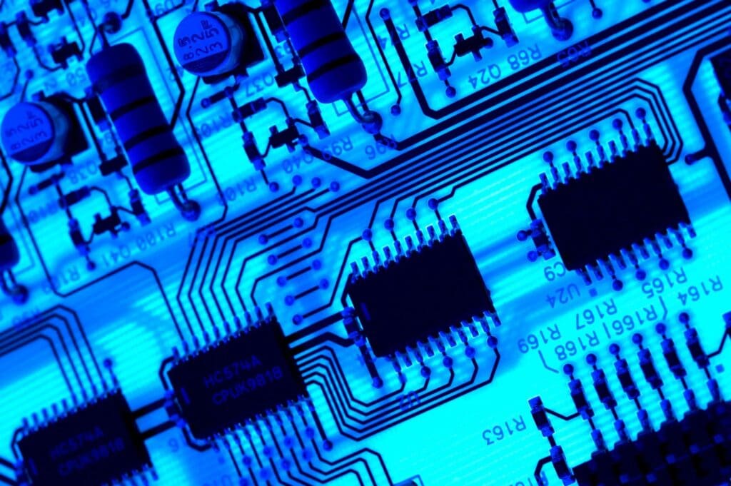 Close-up of a blue-lit circuit board featuring microchips and capacitors, showcasing detailed electronic components.