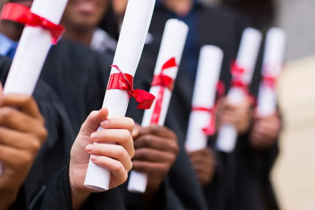 Graduates in black robes holding diplomas with red ribbons, close-up of their hands and diplomas.