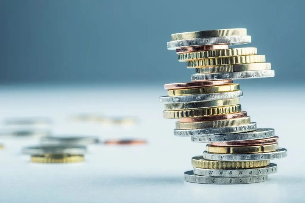 Stack of various international coins arranged in a spiral with several coins scattered around, on a plain light background.