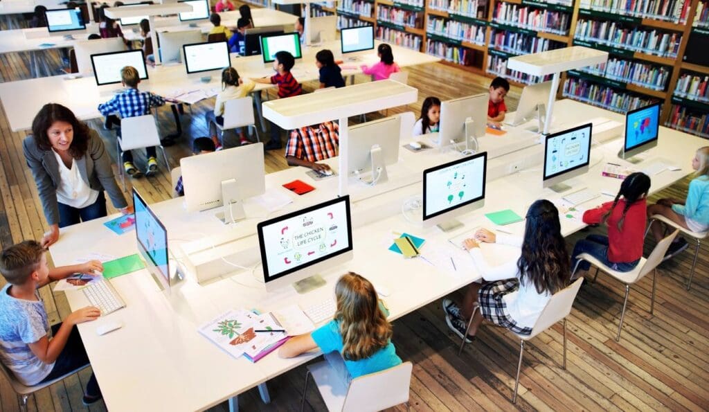 Modern library setting with students of diverse ages using computers and reading, supervised by an adult.