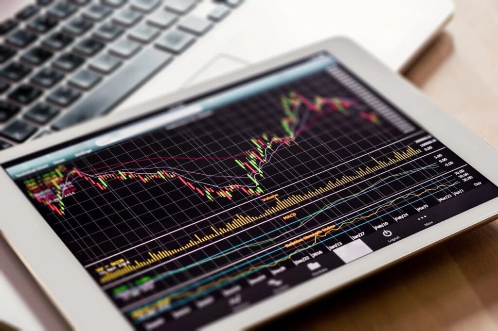 A tablet displaying a detailed stock market chart, with a laptop partially visible in the background.