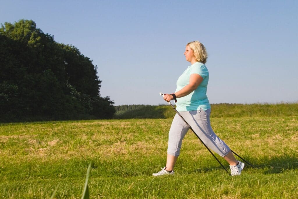 A woman learning about online education while walking in a field using nordic walking poles on a sunny day.