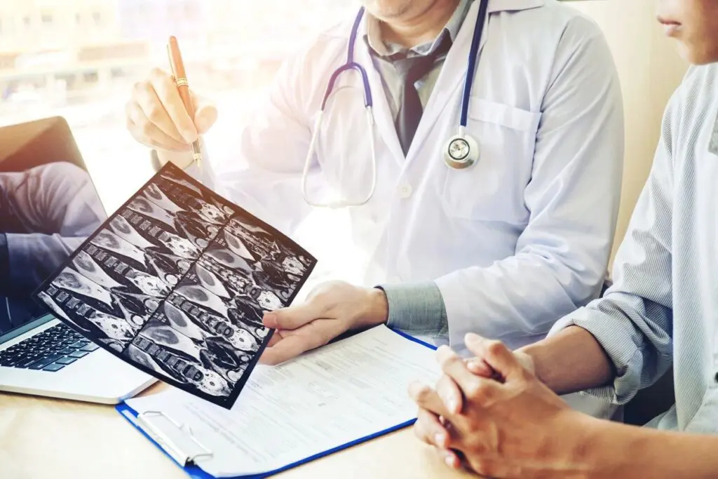 Doctor showing and explaining x-ray images to a patient in an online education session, with a laptop and documents on the table.