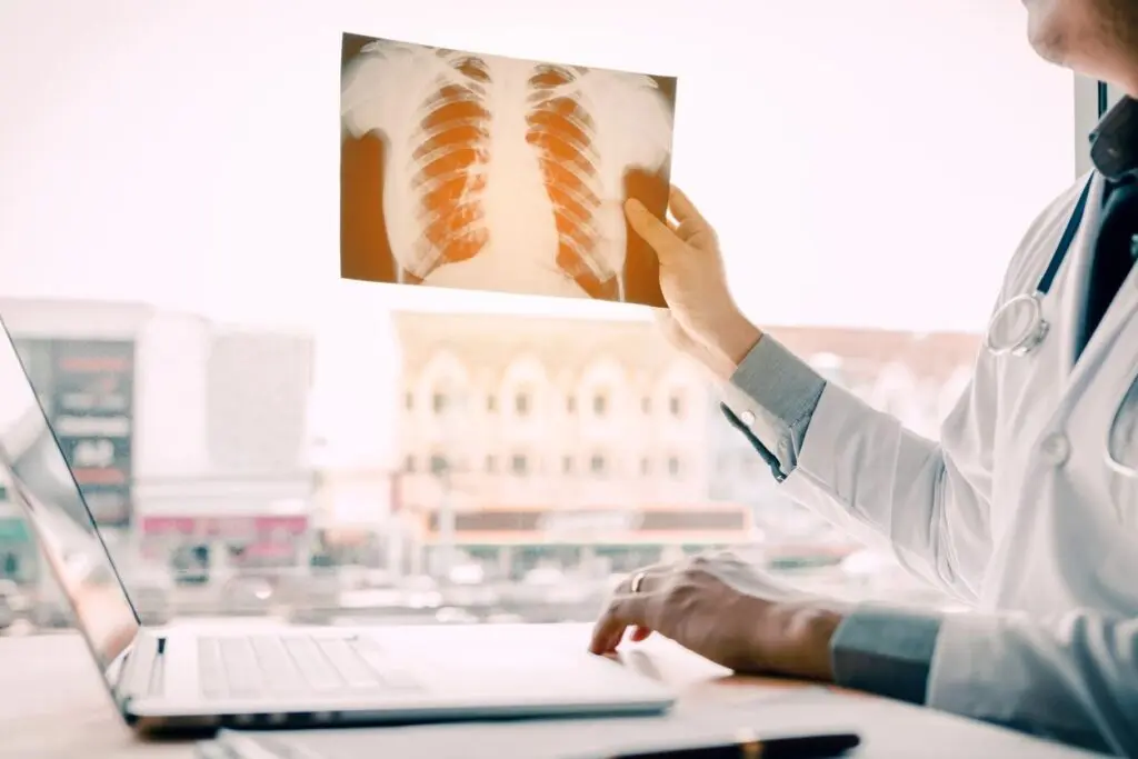 Doctor examining a chest x-ray in a well-lit office with an online education course open on the laptop.