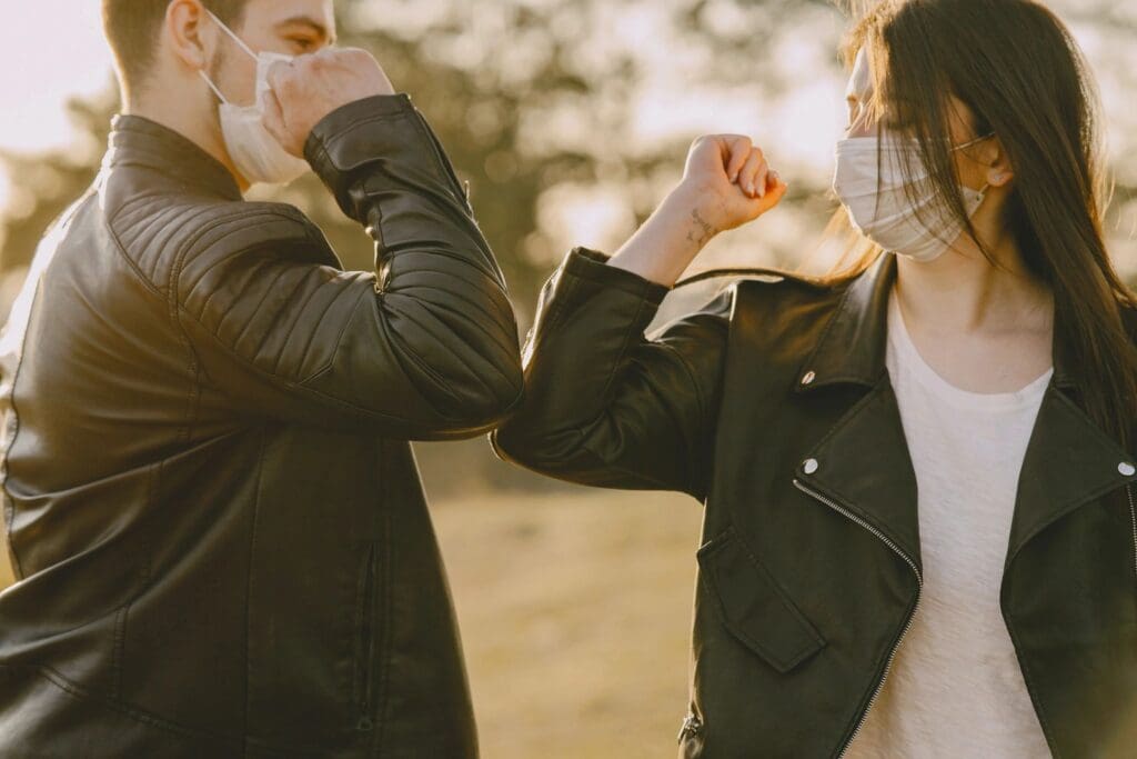 Two people in leather jackets and face masks greeting each other with an elbow bump outdoors at sunset after an online education session.