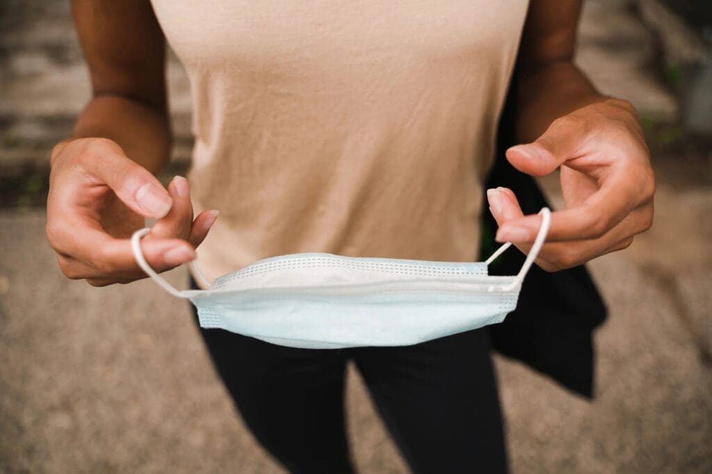 A person holding a surgical mask in front of them, preparing to put it on for an online education session, with a focus on their hands and the mask.