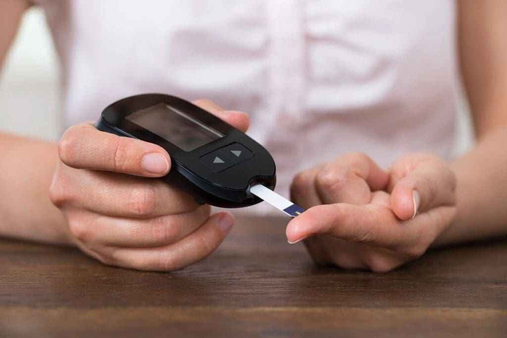 A person using a glucometer to check their blood sugar level by placing a test strip on their finger acquired through an online education course.