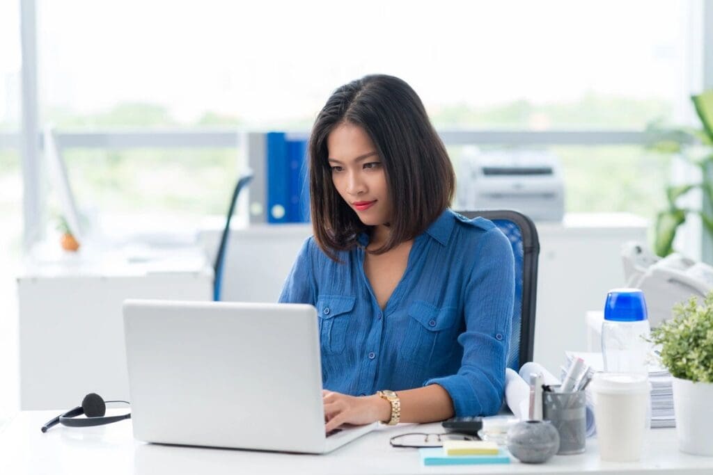 Young woman working on a laptop in a bright office setting.