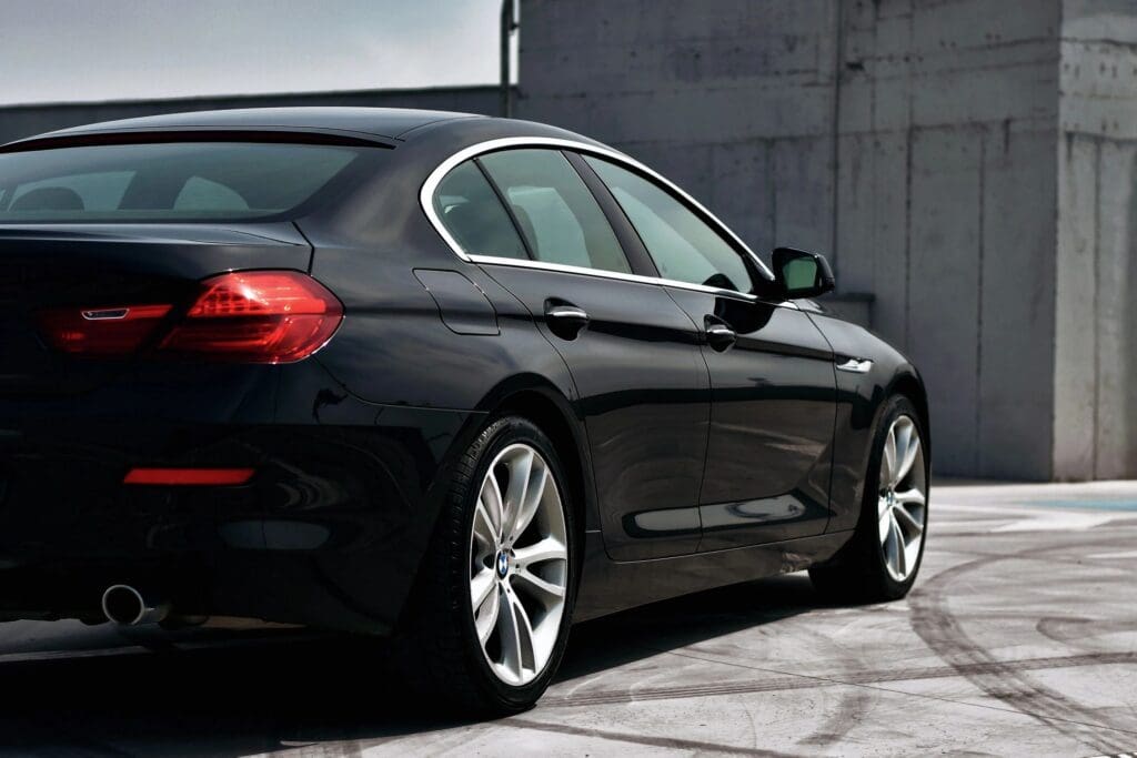 A black luxury sedan parked on a concrete area, showcasing its sleek design and shiny finish.