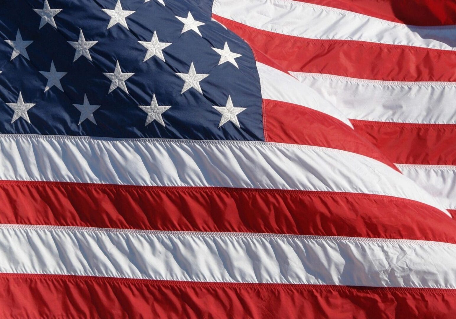 Close-up of the american flag, showing detailed texture of the fabric, with a focus on the stars and stripes in red, white, and blue.