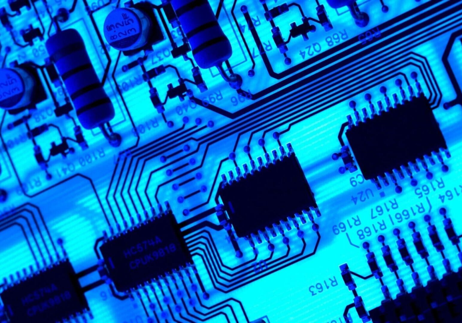 Close-up of a blue-lit circuit board featuring microchips and capacitors, showcasing detailed electronic components.