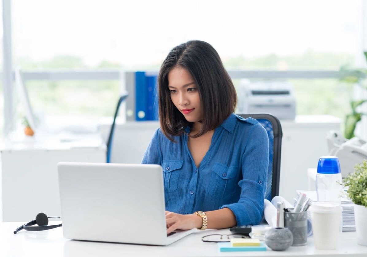 Young woman working on a laptop in a bright office setting.