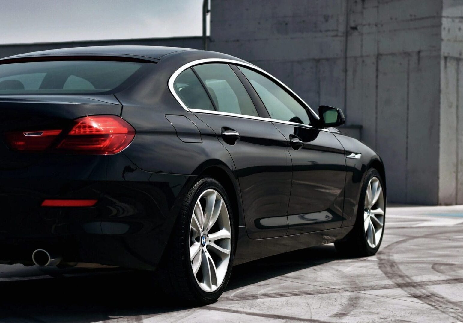 A black luxury sedan parked on a concrete area, showcasing its sleek design and shiny finish.
