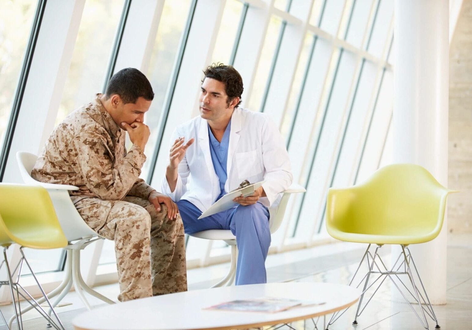A doctor in a white coat consults with a soldier in camouflage uniform about online education in a modern, bright waiting room with large windows.