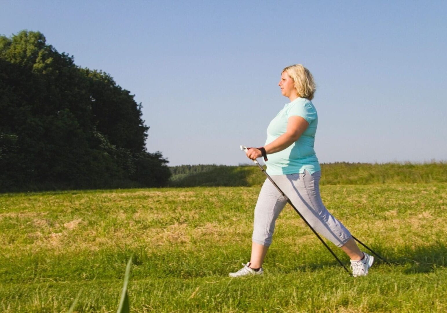 A woman learning about online education while walking in a field using nordic walking poles on a sunny day.