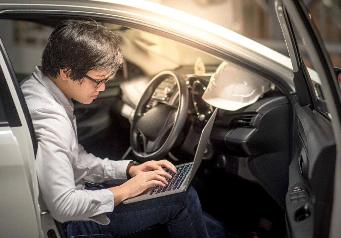 Young Asian Engineer or Architect working with laptop computer while sitting in his car. Mechanical engineering and building construction concepts (Young Asian Engineer or Architect working with laptop computer while sitting in his car. Mechanical eng