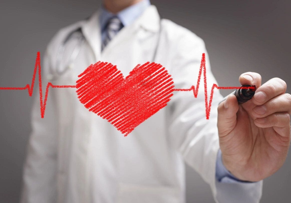 A doctor in a white coat drawing a red heart connected to an ekg line on a transparent surface during an online education session.