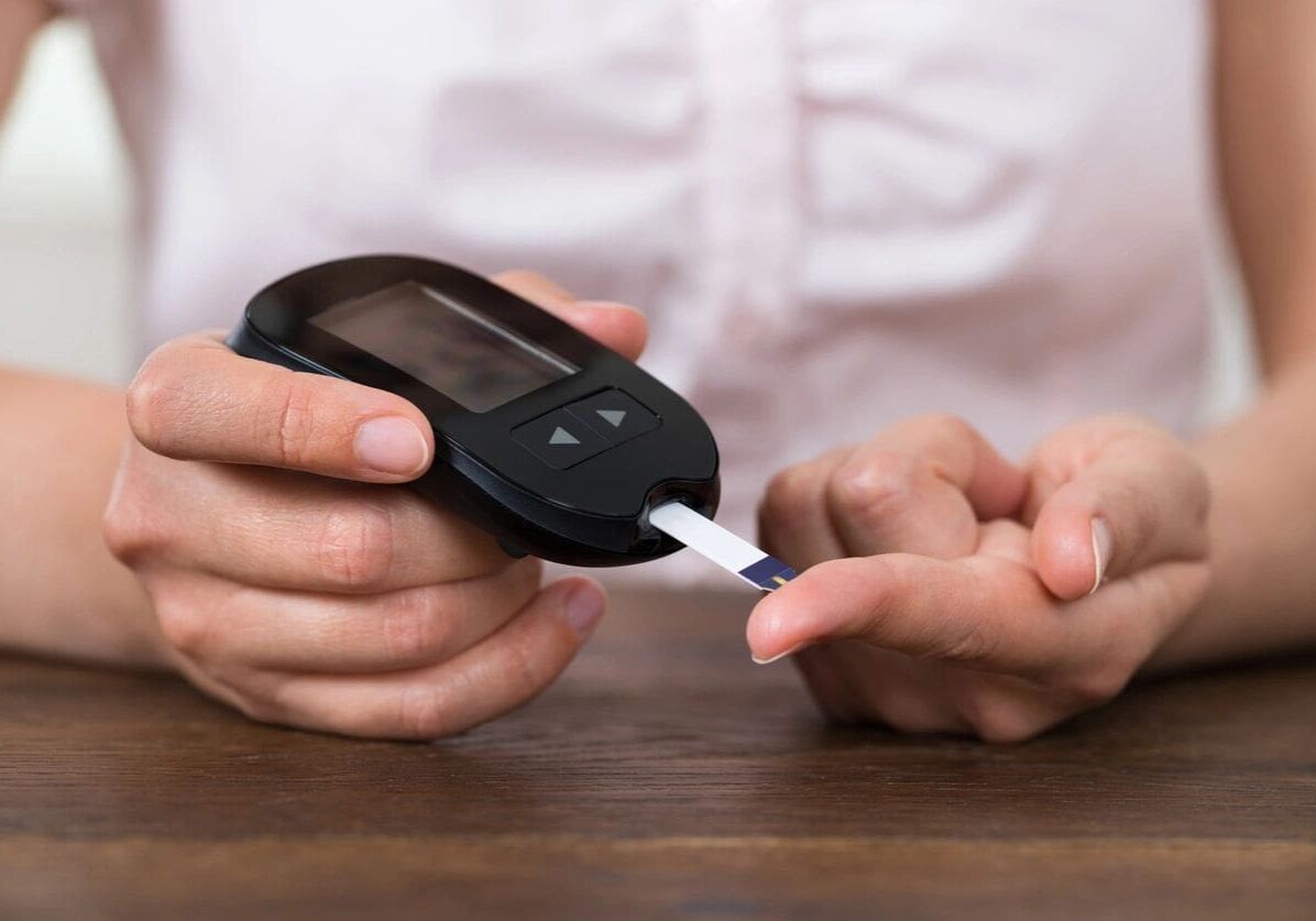 A person using a glucometer to check their blood sugar level by placing a test strip on their finger acquired through an online education course.