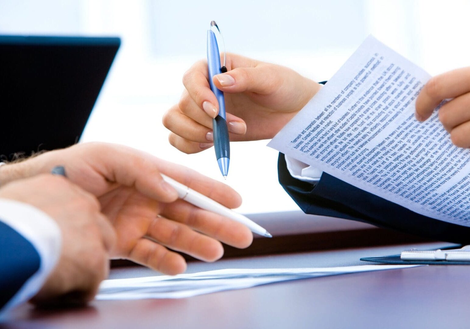 Two business professionals discussing a document at a desk, one handing over a pen for the other to sign.
